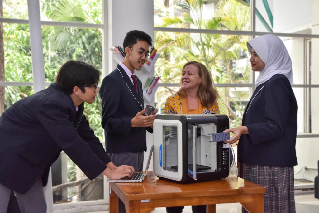 One teacher and three students of IB Middle Years Programme in Sekolah Victory Plus are talking in front of a 3d printer